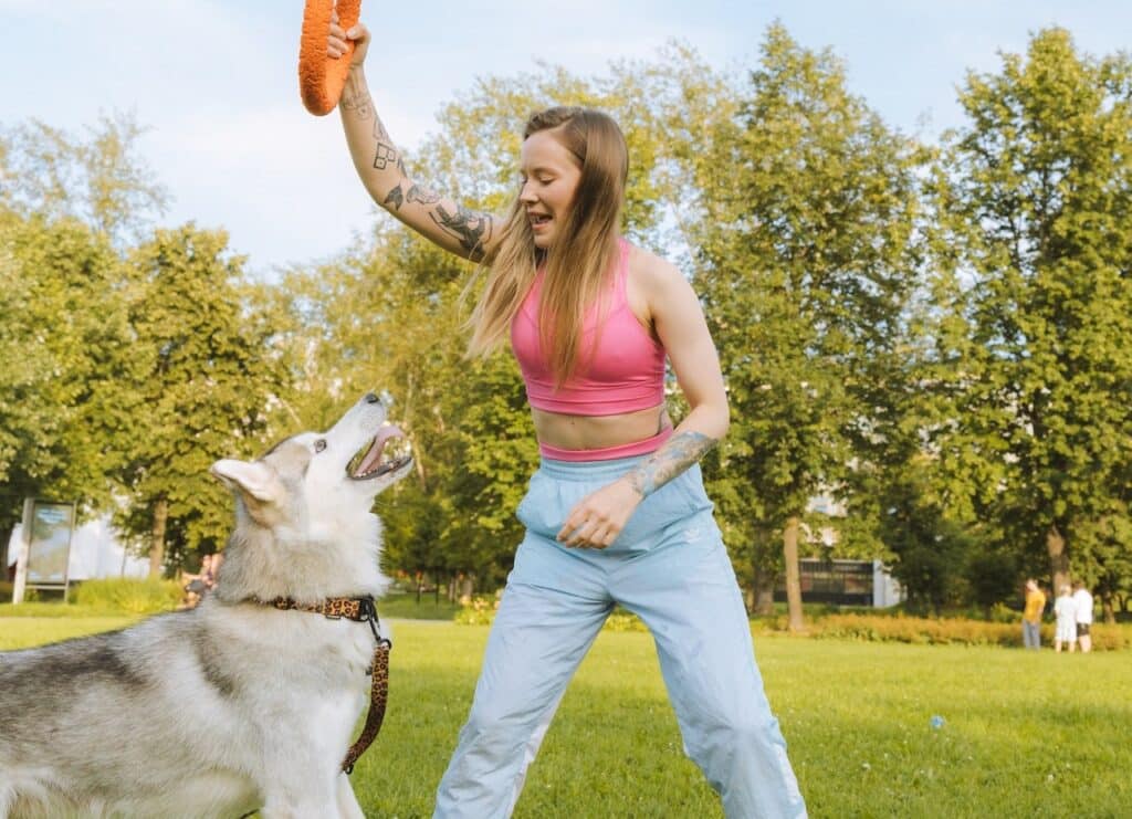 a woman plays with her dog in the park and uses the experience to practice positive reinforcement dog training