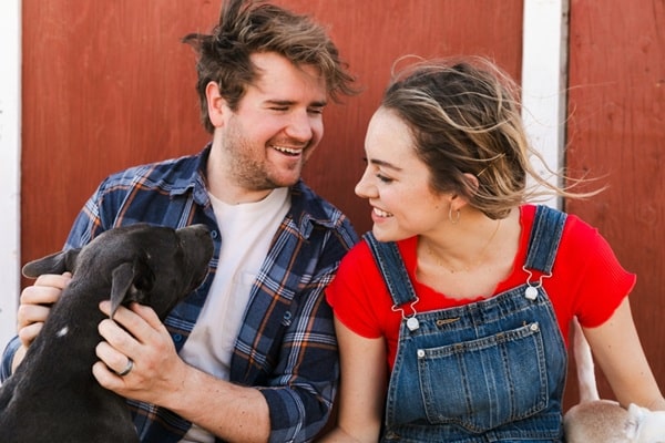 A man and woman sit together outside, smiling at each other while the man pets a black dog, happily discussing their pet claims.