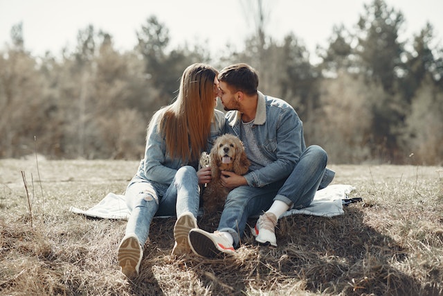 A young couple affectionately cuddling their dog in a field.