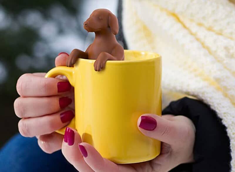 A person holding a yellow mug with a dog figurine that brews tea, perfect for presents for dog lovers.