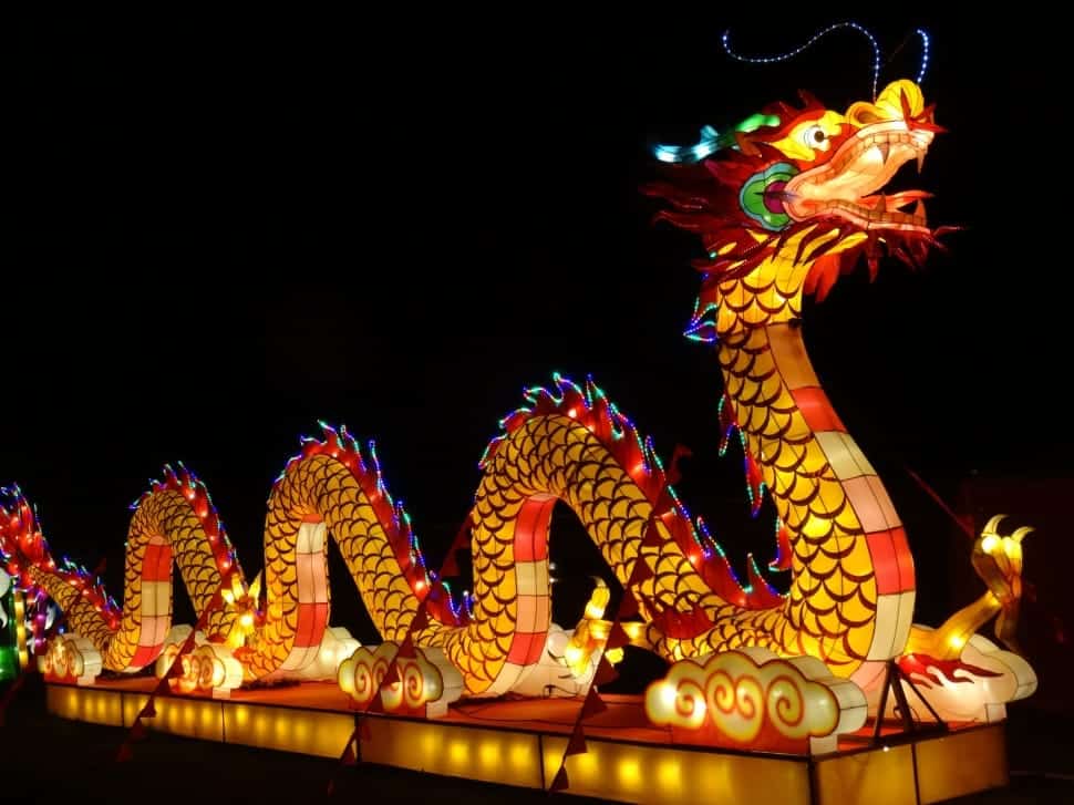 An illuminated dragon lantern with vibrant colors and intricate details shines brilliantly against a dark background, celebrating the spirit of Chinese New Year.