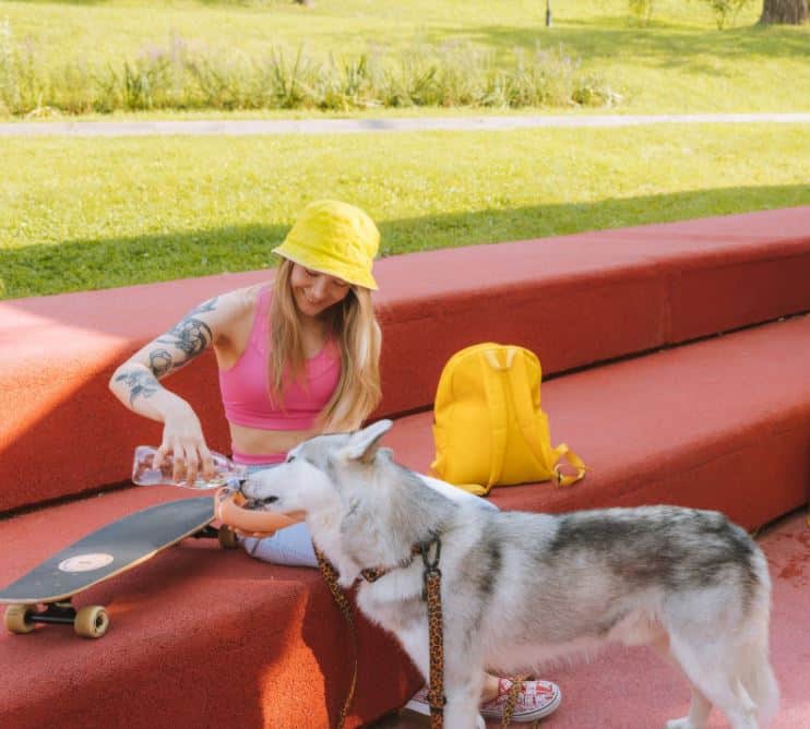 pet safety in summer is on the mind of this girl in a yellow hat playing with her dog in the shade because she knows how to keep pets safe in summer