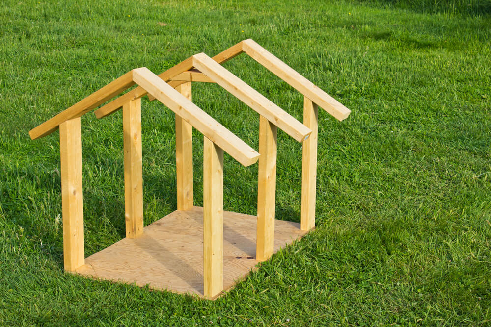 A wooden garden structure, similar to an incomplete house frame on grass, serves as inspiration for your next DIY dog kennel project.