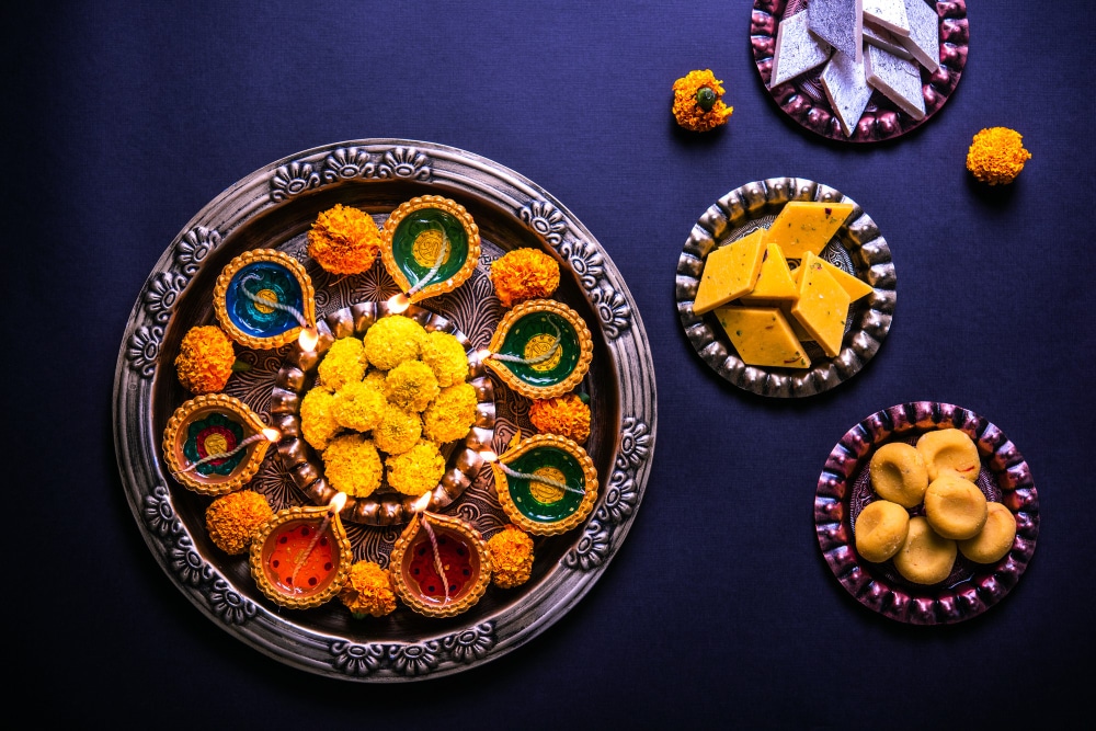 A flower rangoli with sweets, mithai and diya in bowls for Diwali 2024. Make sure to read up on dogs and fireworks and keeping your pets safe during the Diwali fireworks.
