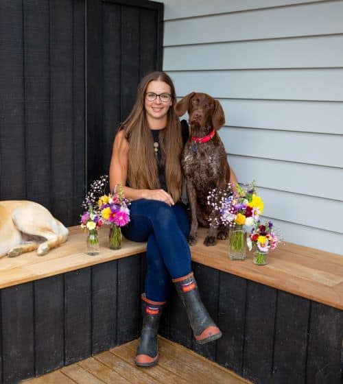 Jacqui Whelan, PD Pet Insurance BDM sits with her dogs amidst flowers that she's grown