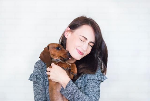 Woman In Grey Top Hugging Brown Dachshund. Whether you're a dog mom or a cat mom, here's how to enjoy Mother's Day