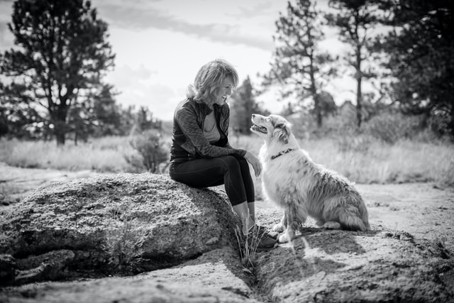 Woman sits side by side her dog alongside a pond. 
