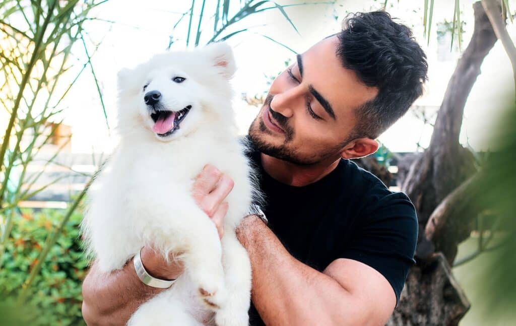 man holds his dog and is happy to have chosen the best pet dental health insurance plans that cover oral health treatments