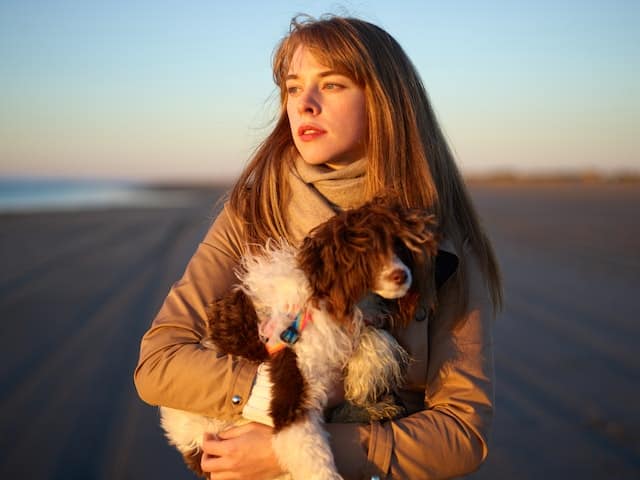 A woman holds her Labradoodle who has been screened for canine cancer as she looks out at the ocean wondering about the test results