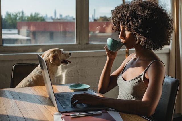 a woman sits drinking coffee and researching the origins of animal insurance while her trusty dog sits by her side