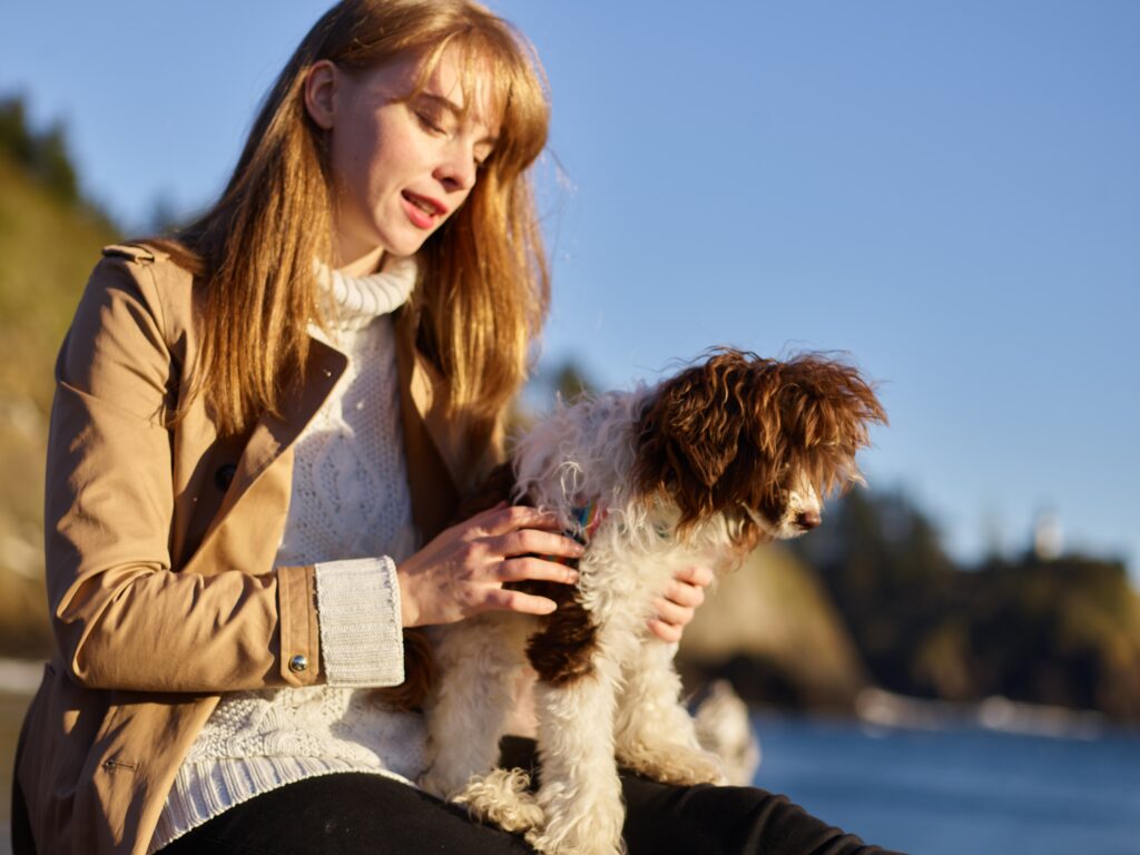 a woman sits with her Labradoodle looking out over the ocean