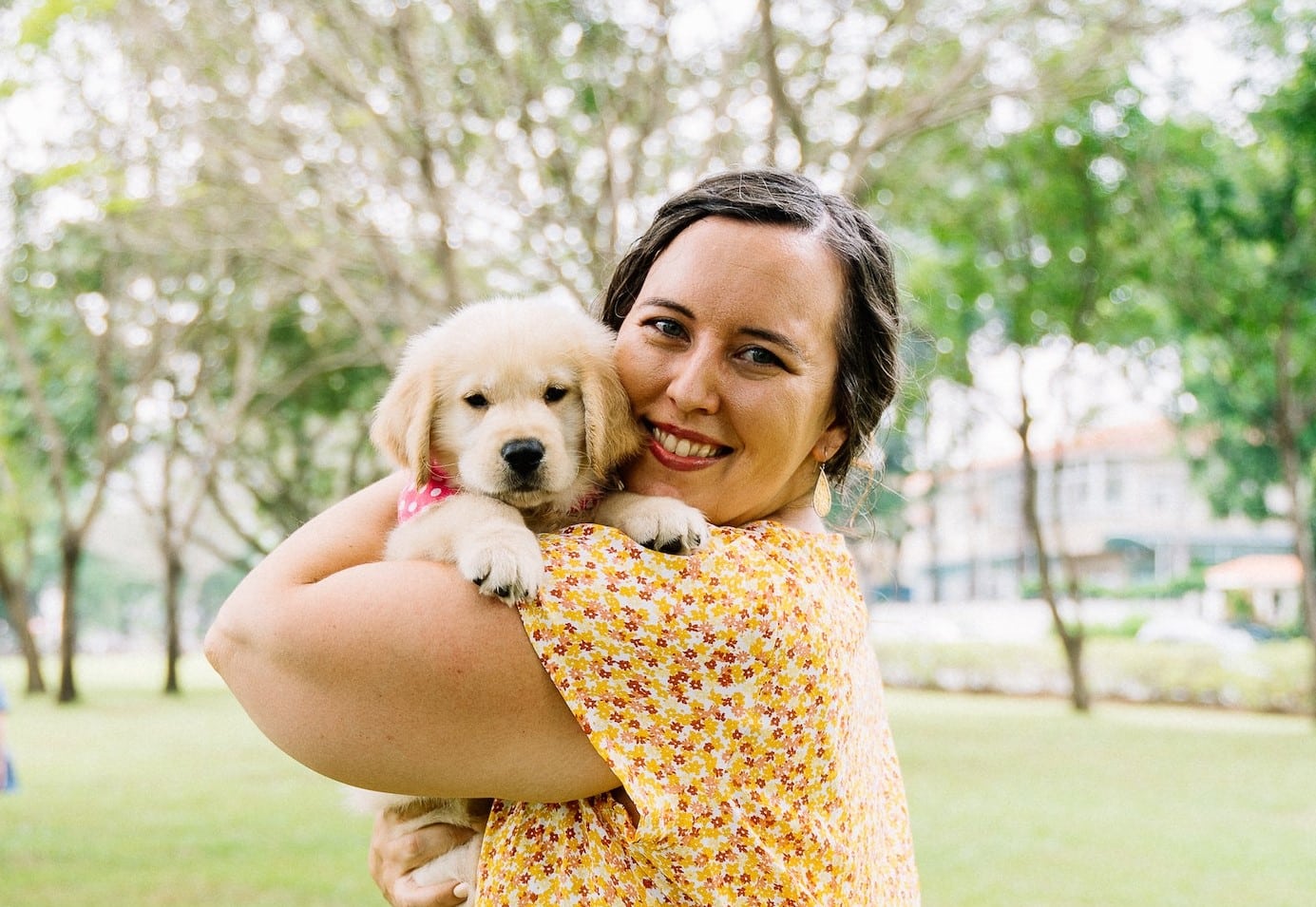 a woman hugs her puppy against the backdrop of a park