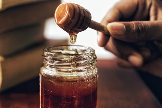 A person is pouring honey into a jar, contemplating what human food is good for dogs