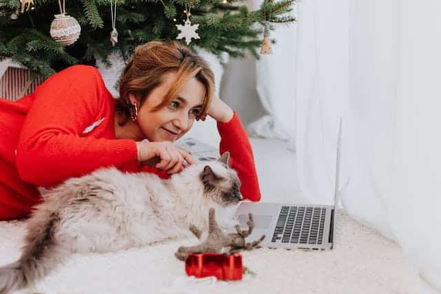 A woman sits with her cat alongside a Christmas tree, Googling great dog and cat Christmas presents
