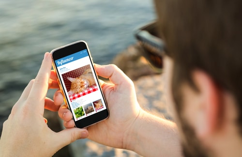 A man holding a cell phone with a picture of furry cat influencer on it.