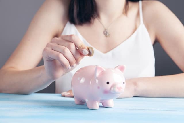 A woman is putting a coin into a piggy bank to save money for unexpected vet expenses for her pet cat but wonders whether she should rather buy pet insurance for a better financial safety net?