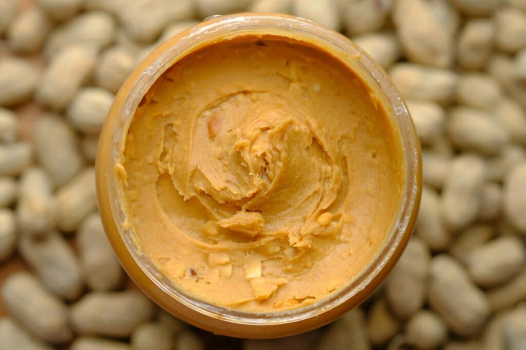 Peanut butter in a jar surrounded by peanuts.
