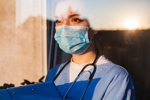 A vet nurse wearing a surgical mask, holds a clipboard in front of a window as she considers the treatment her dog patient will need based off its diagnosis