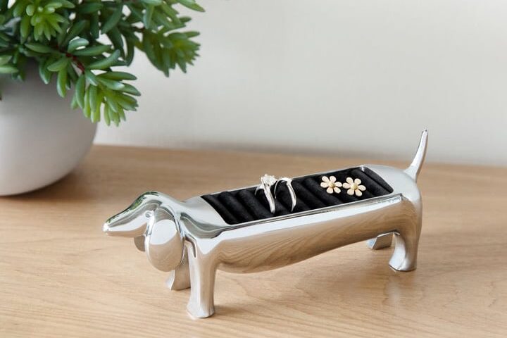 A silver dog-shaped jewellery holder sits on a table.