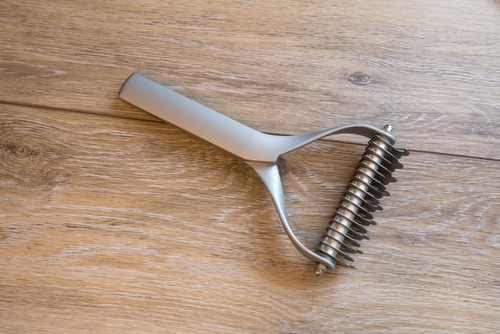 A metal hair comb for shedding on a wooden floor.