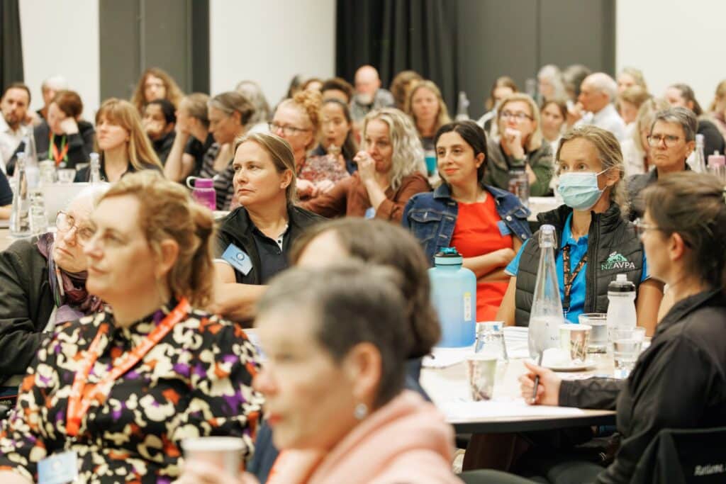 Audience members attentively listening at the CANZ conference event, with some wearing face masks.