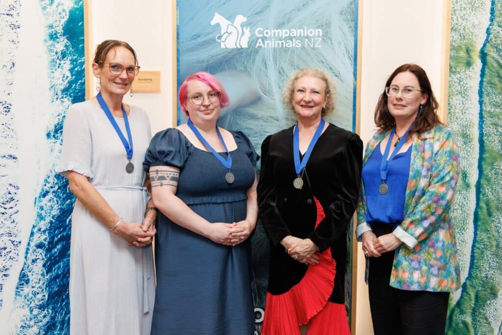 Four individuals with medals standing beside a banner for the Companion Animals NZ conference.