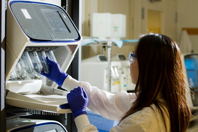 A person in a lab coat and gloves operates a laboratory machine, handling multiple tubes for pet health research at Healthy Pets New Zealand.