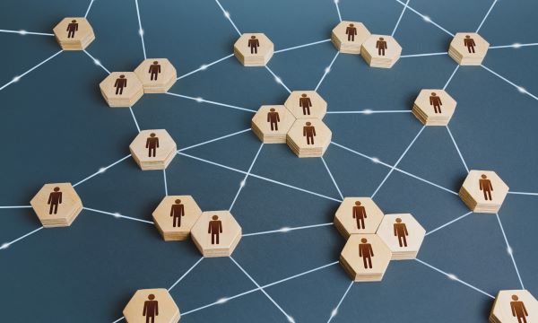 Wooden hexagons with person icons connected by lines, representing a network or organizational structure on a blue background, akin to AI in data science visualizing interconnected systems.