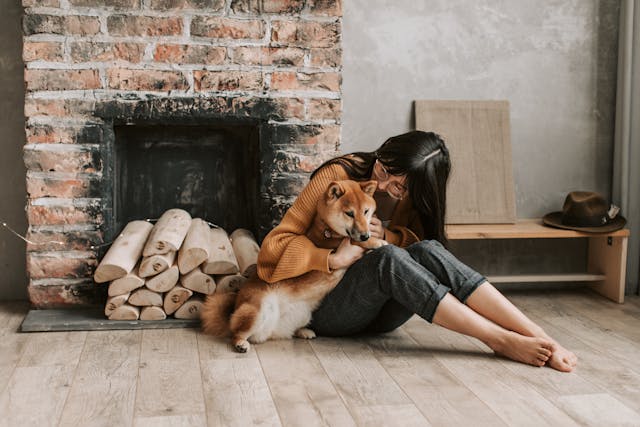 A person sits on the floor beside a fireplace, holding a small dog close as they reminisce about how Cytopoint helped manage the dog's atopic dermatitis.