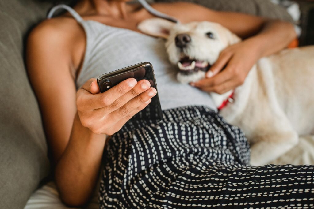 A person lounges on a couch using a smartphone, exploring the best AI apps while their dog rests comfortably beside them.