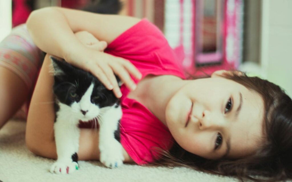 On Pink Shirt Day, a child lies on the floor cuddling a black and white kitten, celebrating kindness and compassion.