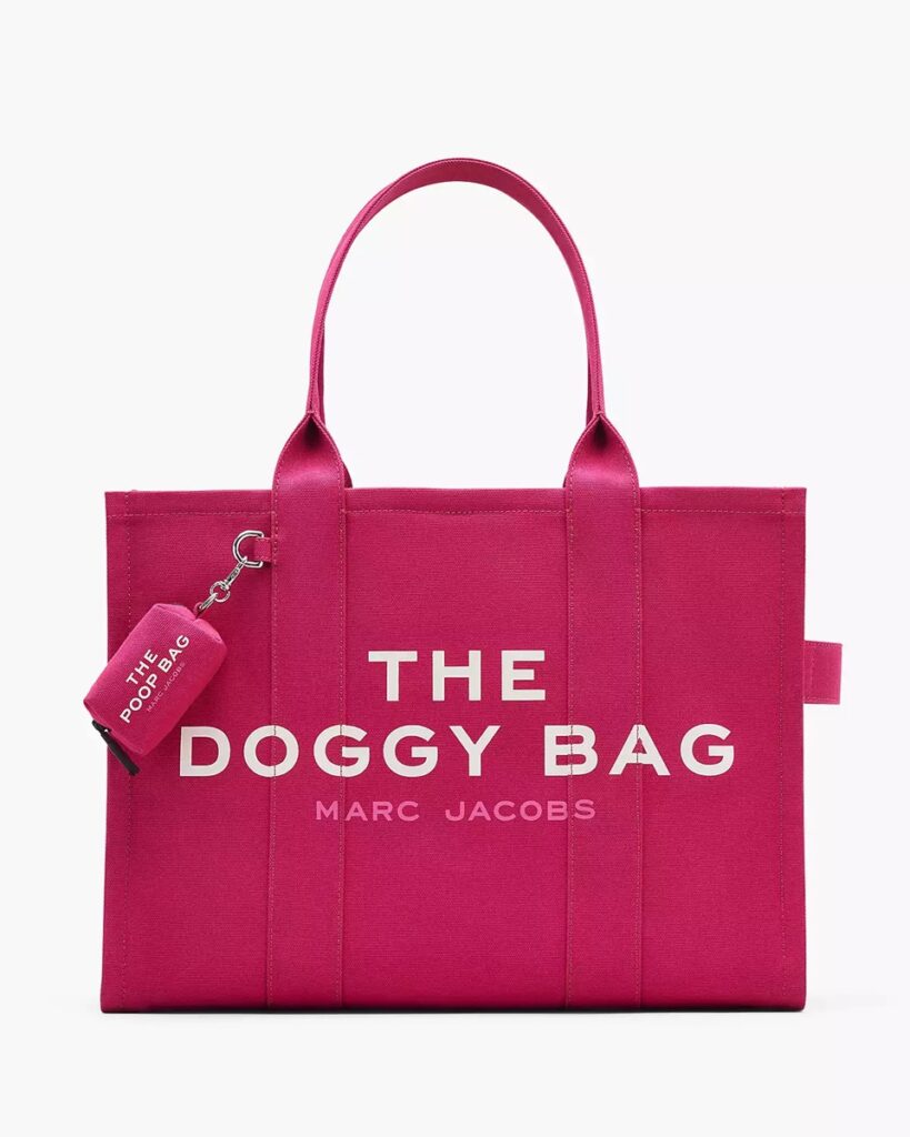 A pink Marc Jacobs tote bag with two handles, labeled "THE DOGGY BAG" in large white letters and a matching pink keychain attached—perfect for carrying dog christmas presents or finding good Christmas gifts for dogs.